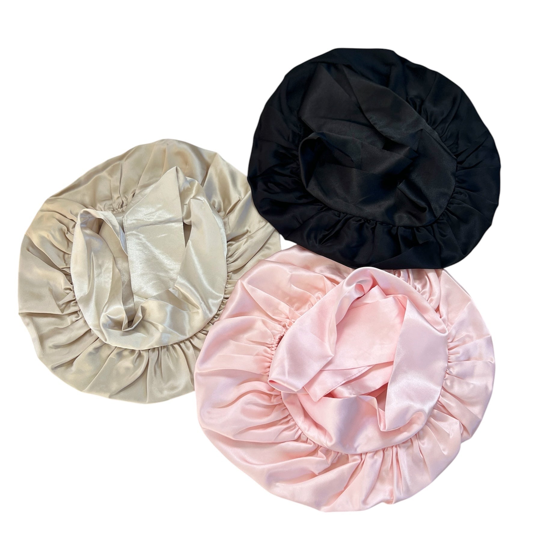Three silk hair bonnets in black, champagne and pink on a white background
