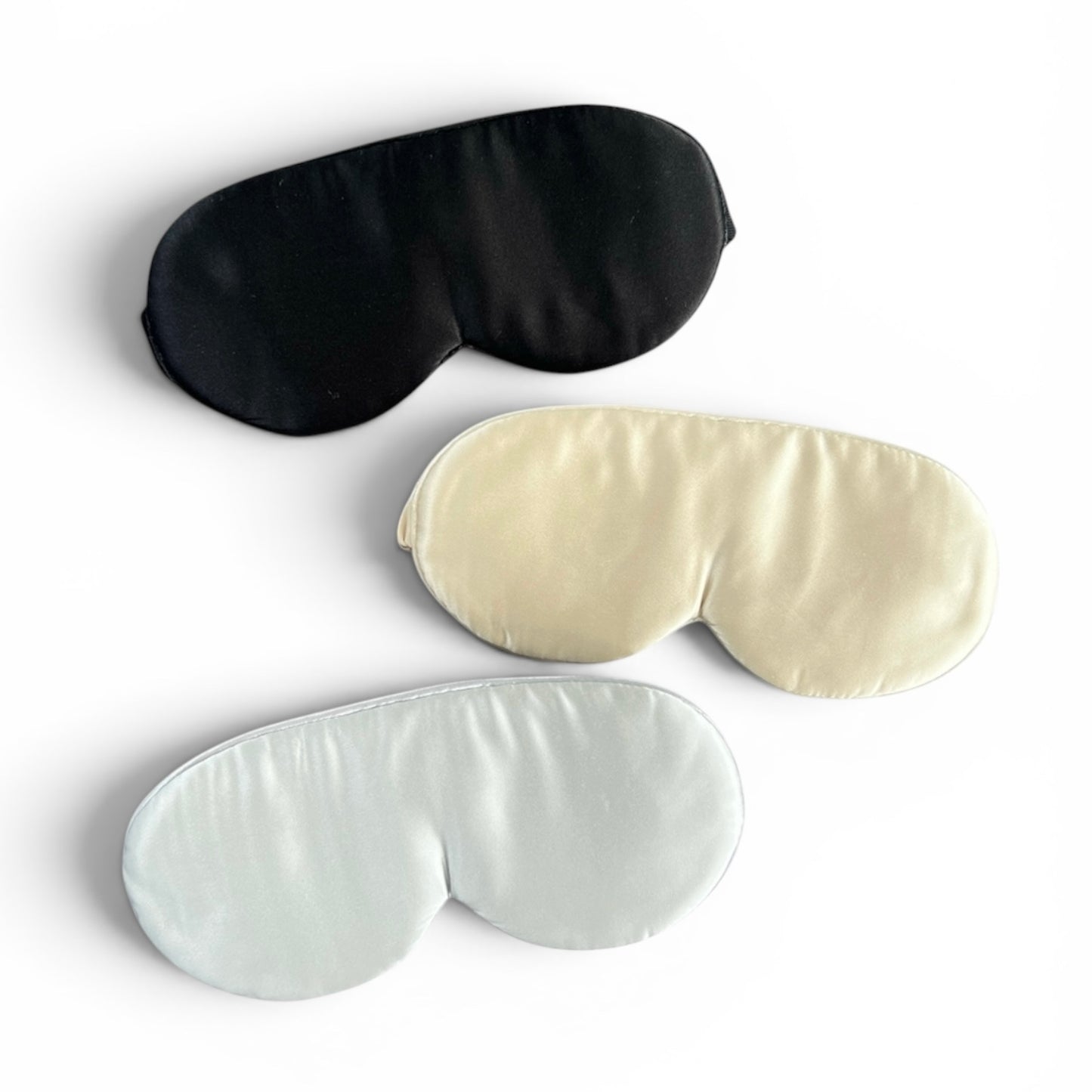 Three eye masks in black, champagne, and silver on a white background
