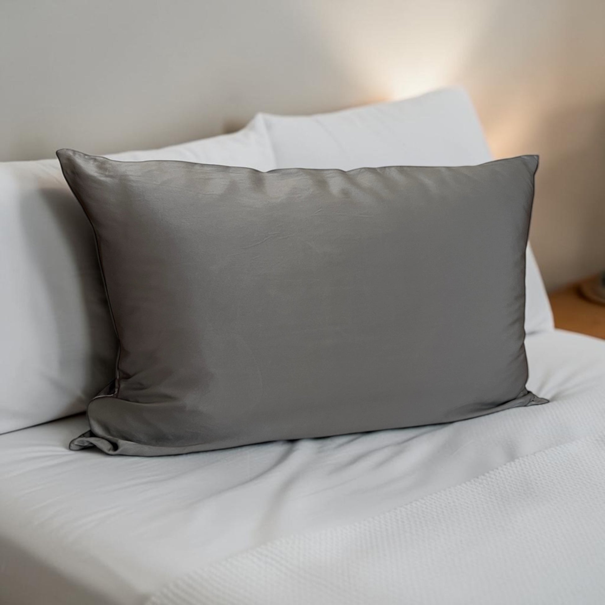 Gray silk pillow on a bed with white pillows and bedding.