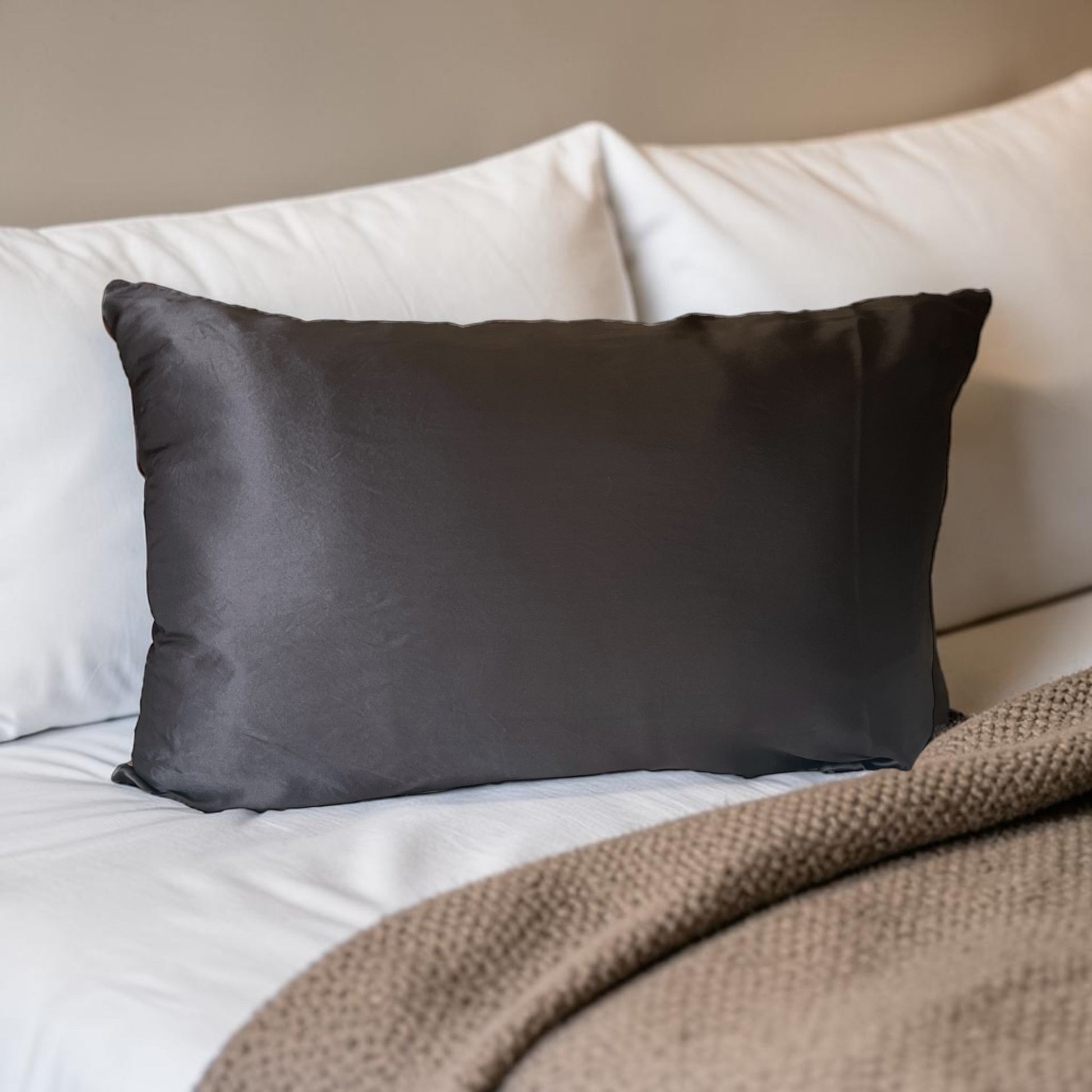 Charcoal pillow on a bed with white bedding and a brown blanket.