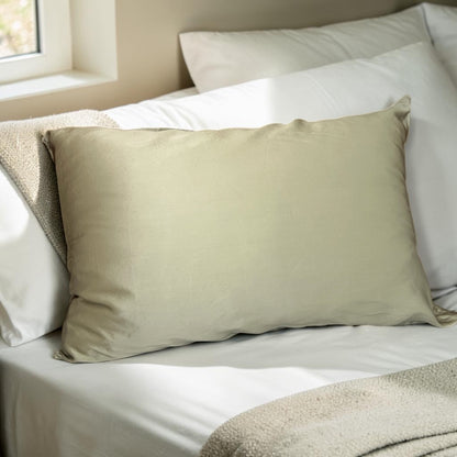 Sage silk pillow on a bed with white bedding and neutral tones.