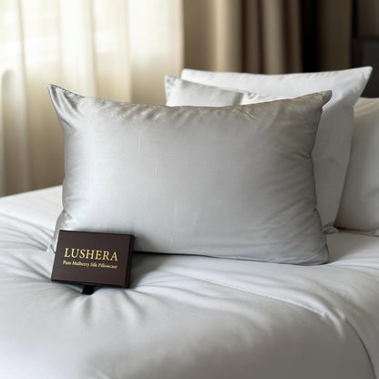 Silver silk pillowcase on a bed with 'Lushera' packaging in the foreground