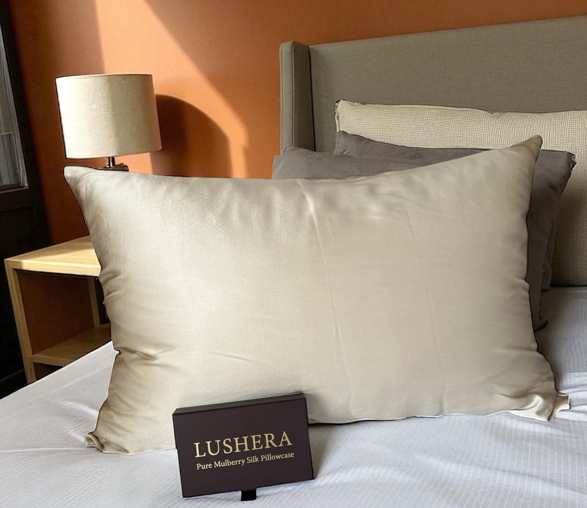 Champagne pillowcase on a bed with 'Lushera' packaging in front, against an orange wall.