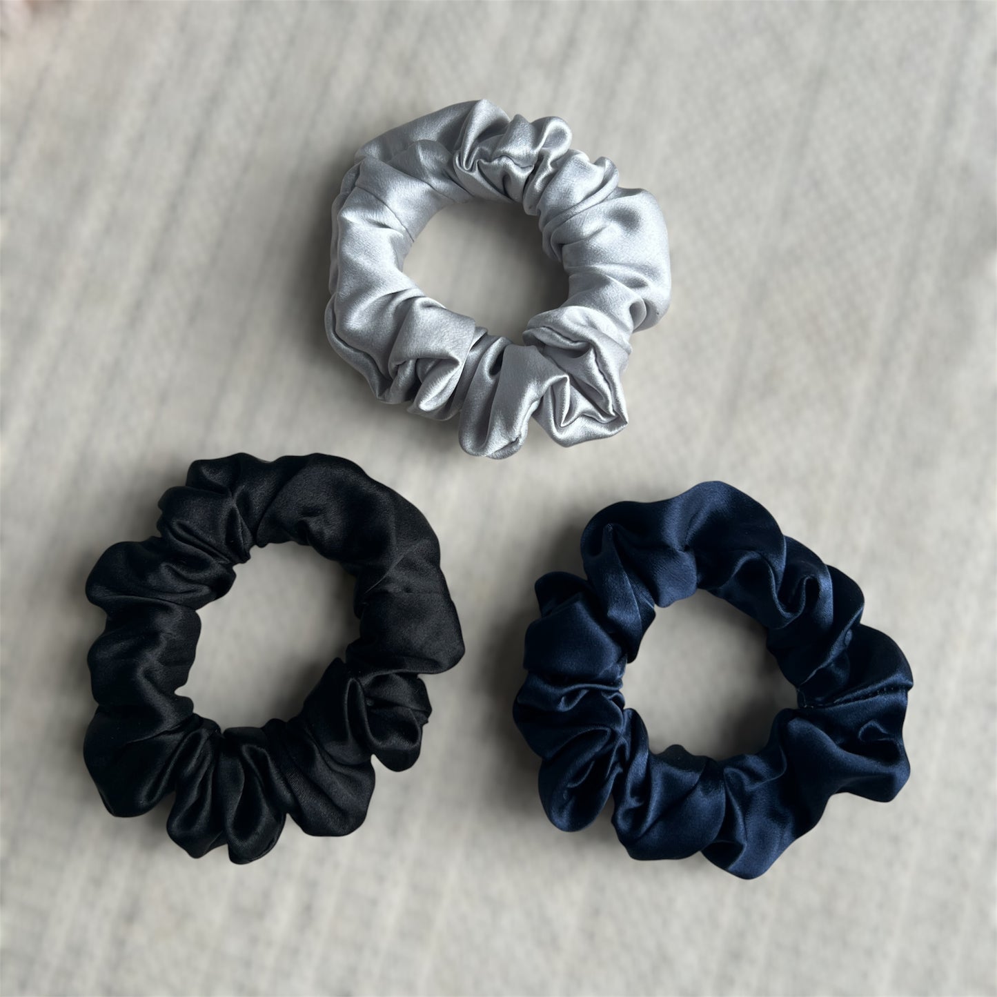 Three scrunchies in silver, black, and navy on a textured surface